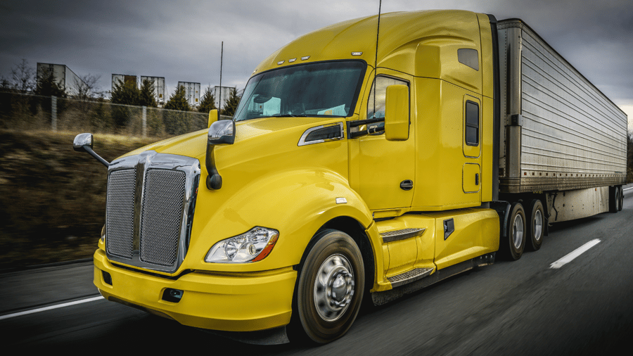 Bright yellow semi-truck and refrigerated trailer on an American highway. 