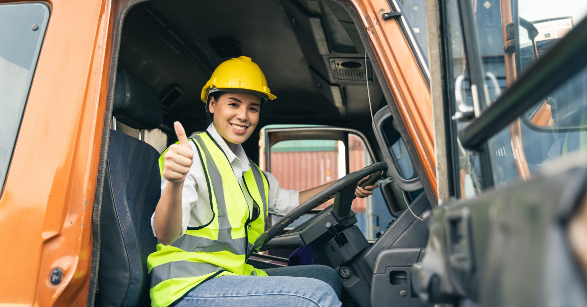 Happy truck driver with thumbs up sitting inside the cab of a truck.