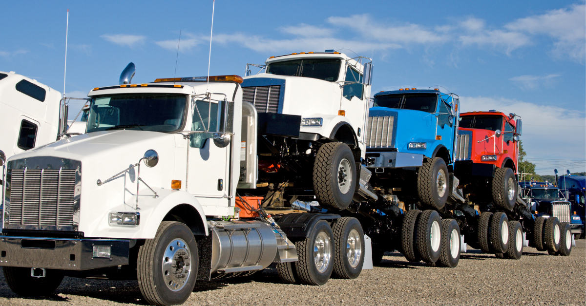 Three new semi trucks being delivered by a white semi truck. 