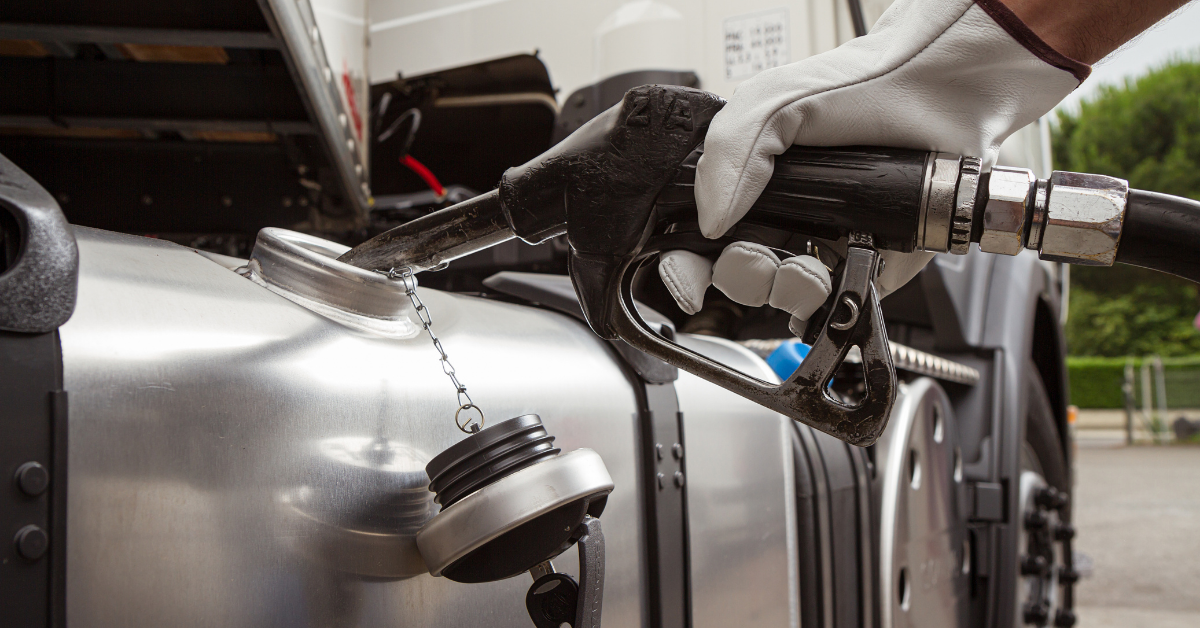 A person wearing a white glove pumping fuel into a silver semi truck. 