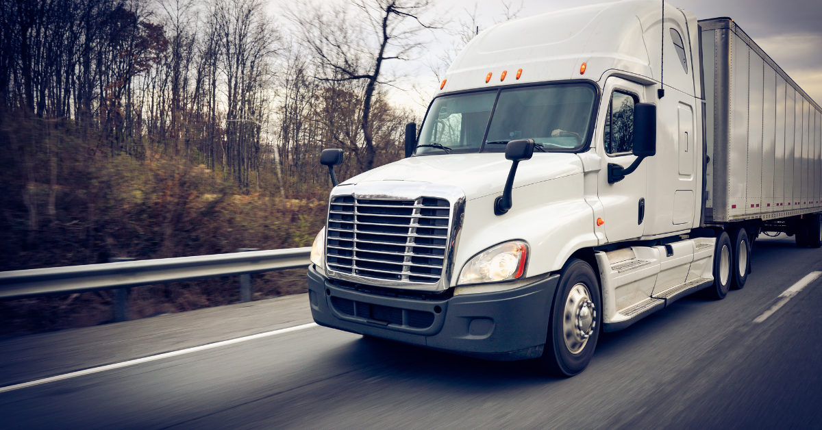 A white semi truck and trailer moving down the highway. 